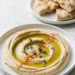 Bestes Hummus Rezept serviert mit Fladenbrot — cremiger Kichererbsen-Dip stilvoll inszeniert auf weißem Marmor