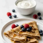 Haferflocken-Crepes serviert mit griechischem Joghurt — gesundes, leichtes Frühstückssetting auf Marmor