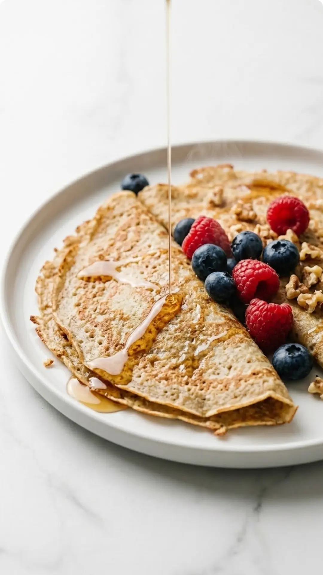 Haferflocken-Crepes frisch gebacken — hauchzarte, gesunde Crepes serviert mit frischen Beeren und Ahornsirup