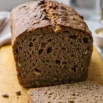 Schnelles Kürbiskernbrot frisch gebacken — matte, dunkelbraune Kruste und saftiges Kastenbrot auf gelbem Brett