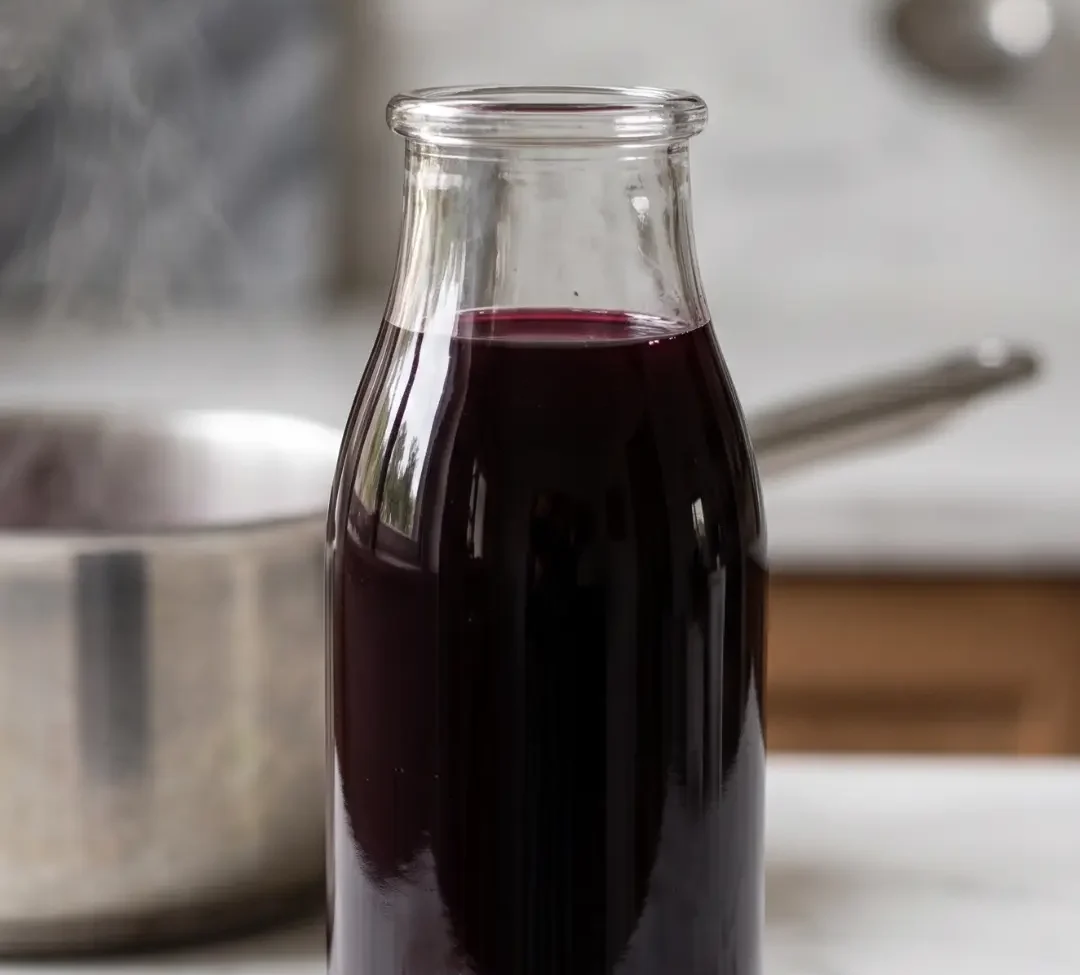 Holundersaft ohne Zuckerzusatz selber machen frisch zubereitet — tiefvioletter Saft in Glasflasche